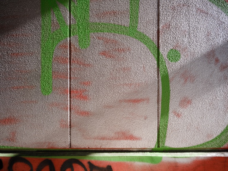 Graffiti on an elevated wall. The rough concrete wall surface is clearly visible in the morning sunlight.