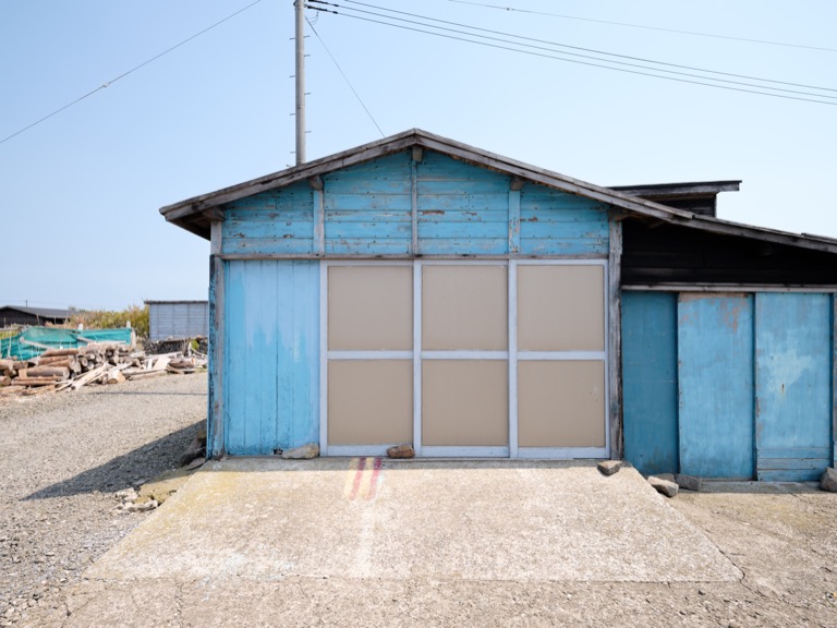 A light blue wooden warehouse under a blue May sky. A stone on the rail of the sliding door.